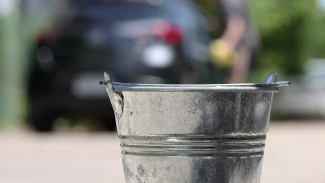 A man washes a car on the street, then throws a sponge into a distant bucket with splash of detergent, slow motion. A domestic hand washing car with soapy water.