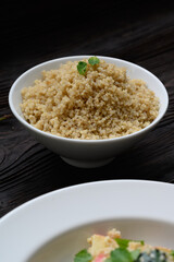 Bowl of boiled quinoa on wood background