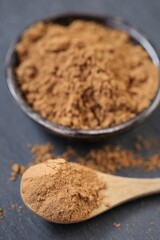 Guarana powder in a wooden spoon and a ceramic cup on a black slate background.Brown guarana powder texture. Healthy eating.Natural energetic.Useful product.