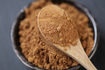 Guarana powder in a wooden spoon and a ceramic cup on a black slate background.Brown shredded guarana powder texture. Healthy eating.Natural energetic.