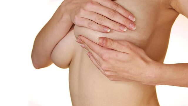 Close-up of a woman's enormous breasts with her hands nipples covered during a BSE (breast self exam).