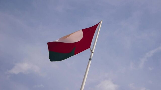 Flag of Oman fluttering in the wind in slow motion with blue sky in the background in Muscat Oman.