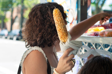 woman holding elote, mexican street corn on the cob with cotija cheese, chili and lime  