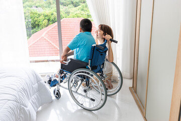 asian woman taking care disabled child on wheelchair in bedroom. both looking at something beside of window.