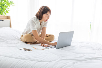 Fototapeta na wymiar asian business woman work from home via laptop on bed with smartphone and notebook.