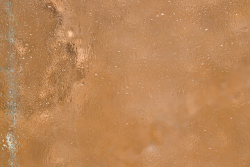 Fototapeta premium Texture. A fragment of a glass surface covered with a thin layer of melting ice is located on a light brown background. Close-up.