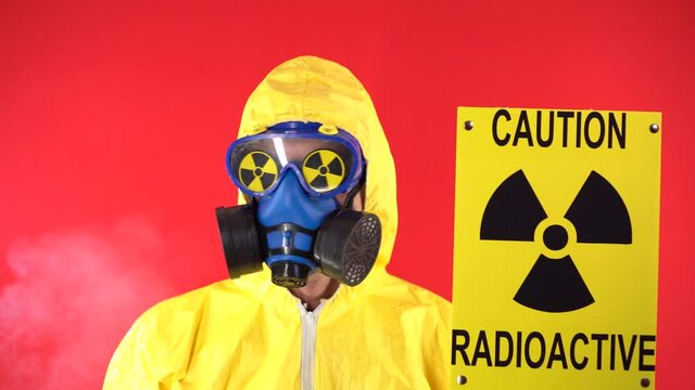Man in Yellow Protective Suit, Protective Mask with Poster Caution radiation shakes its head negatively. Behind the man are couples wearing glasses with radiation signs. Radiation concept.