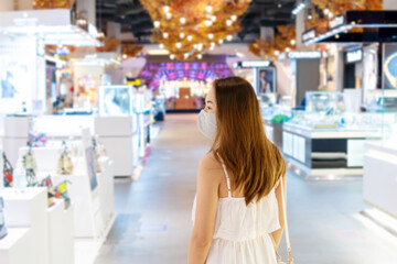 Fototapeta na wymiar Beautiful young Asian woman in white dress with face mask walking at shopping center or department store, blur background, Shopping, new normal lifestyle concept