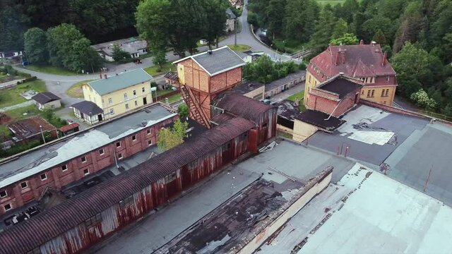 Top view of a drone circling around a giant old lost place factory in the woods with a demolished roof in the middle of nowhere