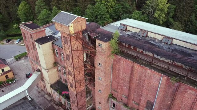 Aerial footage of a drone circling around an abandoned large old socialist factory brick building in the middle of Germany