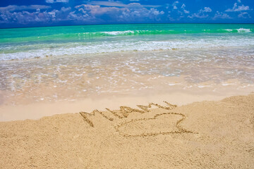 Tropical beach in Miami with bright blue sky, turquoise water and writing on the sand