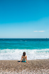 A girl in a bathing suit sits on the beach and looks at the sea