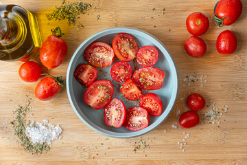 Naples, Italy. Food image of a bunch of tomatoes in a little turquoise bowl on a wooden cutting board with coarse salt, oregano and a glass oil cruet with olive oil.