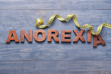 Word ANOREXIA with measuring tape on color wooden background
