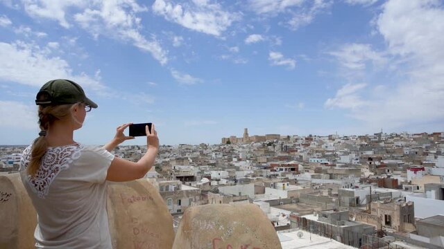 White woman takes pictures of beautiful cityscapes of Tunisian city using digital camera of mobile cellphone.