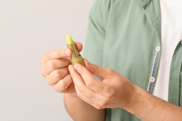 Handsome young man with lip balm on light background, closeup