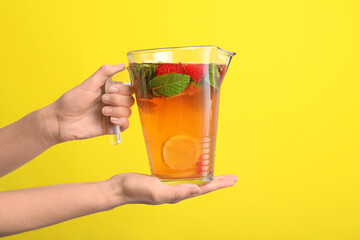 Hand with jug of fresh strawberry lemonade on color background