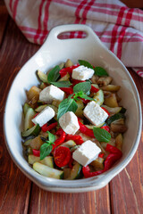 Ratatouille, backed vegetable with feta cheese and fresh basil in white oven pan on wooden brown background, selective focus vertical.