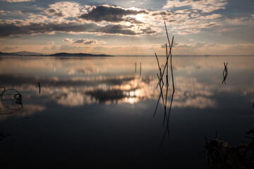 Fototapeta na wymiar Sunset a Trasimeno lake (Umbria, Italy), with fishing net poles reflecting on perfectly still water