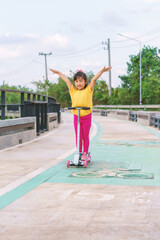Naklejka premium Little child girl to ride scooter in outdoor sports ground on sunny summer day. Active leisure and outdoor sport for children.