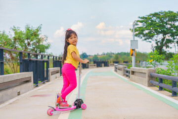 Little child girl to ride scooter in outdoor sports ground on sunny summer day. Active leisure and outdoor sport for children.