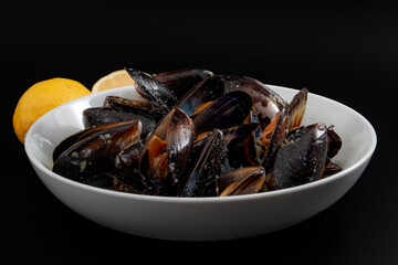 Protein and zinc rich sea food, marine delicacy and luxury foods concept with photograph of a bowl of raw mussels and lemons isolated on black background with clipping path cutout
