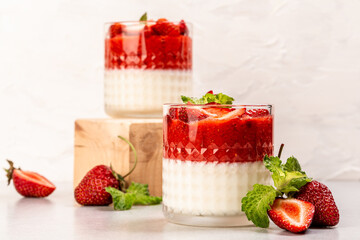 Italian panna cotta dessert with strawberry mousse and mint leaf served in small transparent glasses