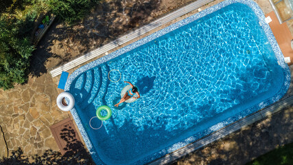Fototapeta na wymiar Aerial view of beautiful girl in swimming pool from above, swim on inflatable ring donut and has fun in water on family vacation on tropical holiday resort 