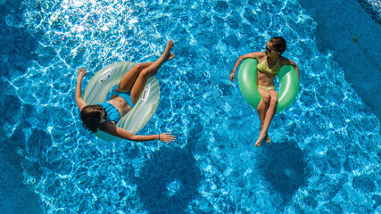 Active children in swimming pool aerial top view from above, happy kids swim on inflatable ring donuts and have fun in water on family holiday vacation on resort
