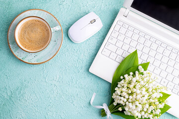 Home office desk table with coffee cup, bouquet of spring flowers lily of the valley flat lay. Workplace with laptop and coffee on feminine background. Blogging, freelance, florist concept. Сopy space