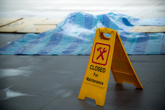 Yellow closed for maintenance sign during rain with puddle of water when floor is slippery and copy space for text
