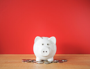 Fototapeta na wymiar White Piggy bank and money coin on wooden desk with red background 