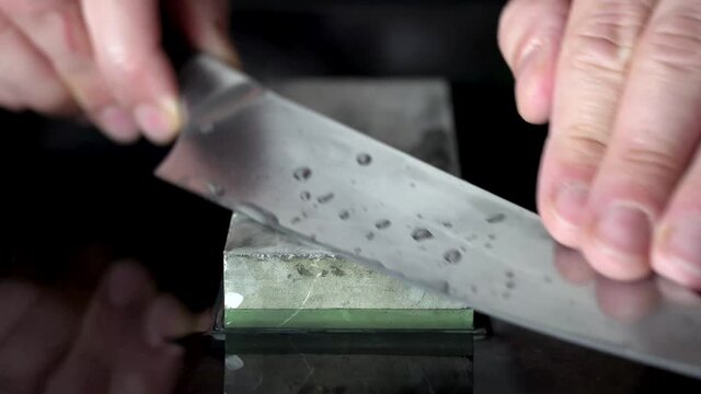Male hands sharpening Japanese chefs knife using whetstone.