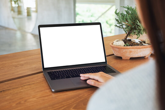 Mockup image of a woman using and touching on laptop computer touchpad with blank white desktop screen on wooden table