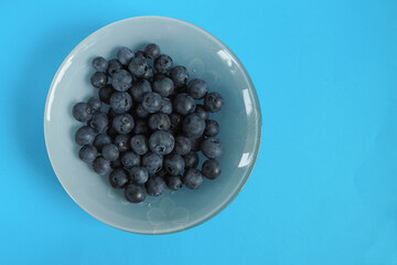 grey glass round plate with blue blueberries on a blue background top view