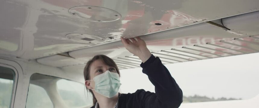 Woman learning for pilot with face mask checking or inspecting small airplane plane aircraft wing during virus covid 19 coronavirus pandemic outbreak new normal