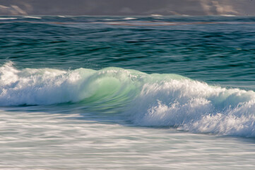 Breaking wave rolling into the sandy beach in Central California