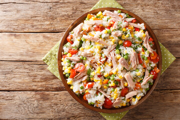 Salad of rice, tuna, tomatoes, sweet pepper, corn, green peas and herbs close-up in a plate on the...