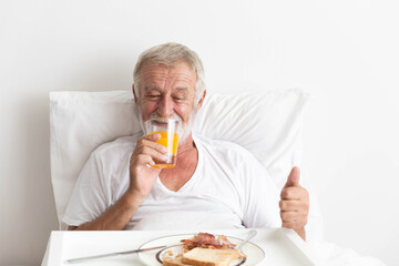 Senior retirement male happy having breakfast with orange juice and water on bed