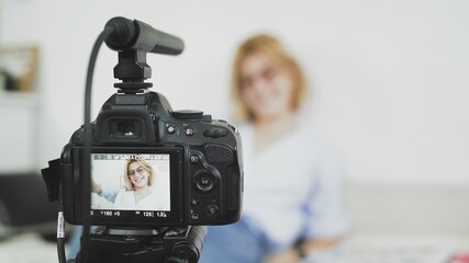 Video camera with microphone on the top is recording video of female blogger