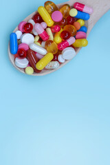 Colorful assorted pharmaceutical medicine capsules , tablets and pills in wooden spoon isolated on blue background. Dietary supplement healthcare product.Copy space for text.