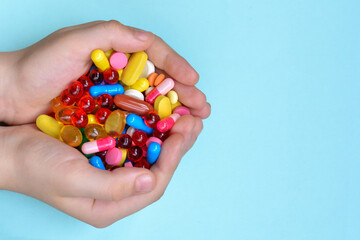 Child's hands hold many colorful vitamins, capsules, supplements, pills.