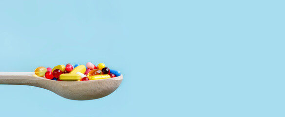 Colorful assorted pharmaceutical medicine capsules , tablets and pills in wooden spoon isolated on blue background. Dietary supplement healthcare product.Copy space for text.Banner