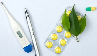 Yellow pills, thermometer and pen on a white background. Cold and flu time.