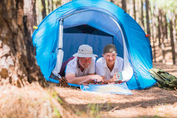 Couple of active traveler senior people enjoy together inside a tent in free camping in the forest - young retired people and free alternative lifestyle concept with love for nature - travel life  - Powered by Adobe