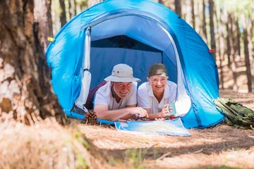 Fotobehang Couple of active traveler senior people enjoy together inside a tent in free camping in the forest - young retired people and free alternative lifestyle concept with love for nature - travel life  © simona
