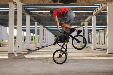 Fototapeta premium Man in color t-shirt on the bike. Bmx rider performing tricks at street with striped shadow from the sun