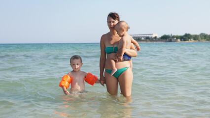Young mother standing in water in sea with two little boys
