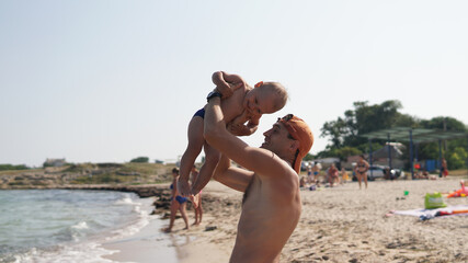 Little happy kid and his smiling father on the beach. Dad lift up boy
