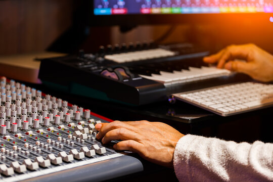 composer hand adjusting audio level on mixing console while arranging music on computer